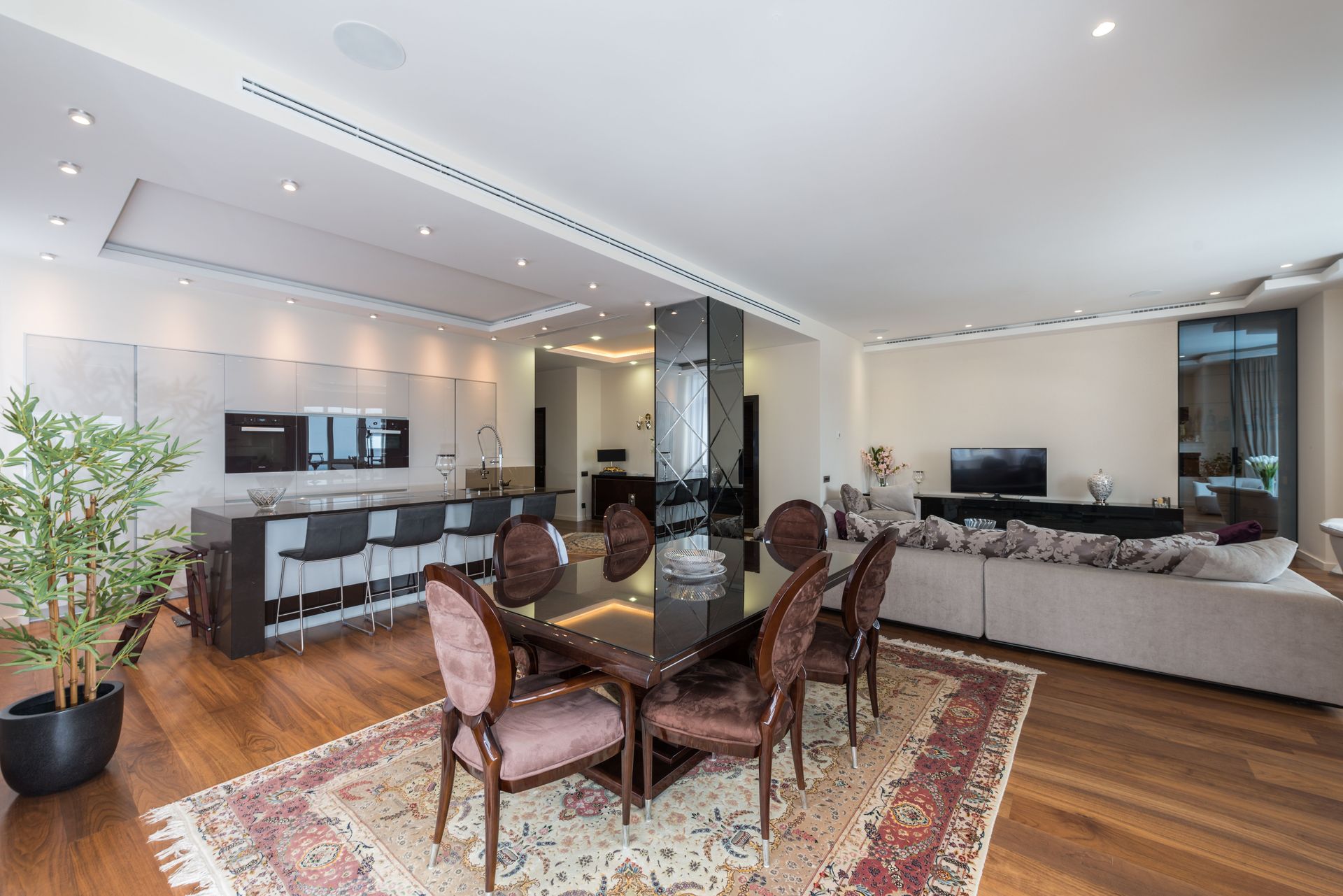 Wooden table with soft chairs placed in spacious classic styled studio apartment with kitchen zone and living room with cozy sofa